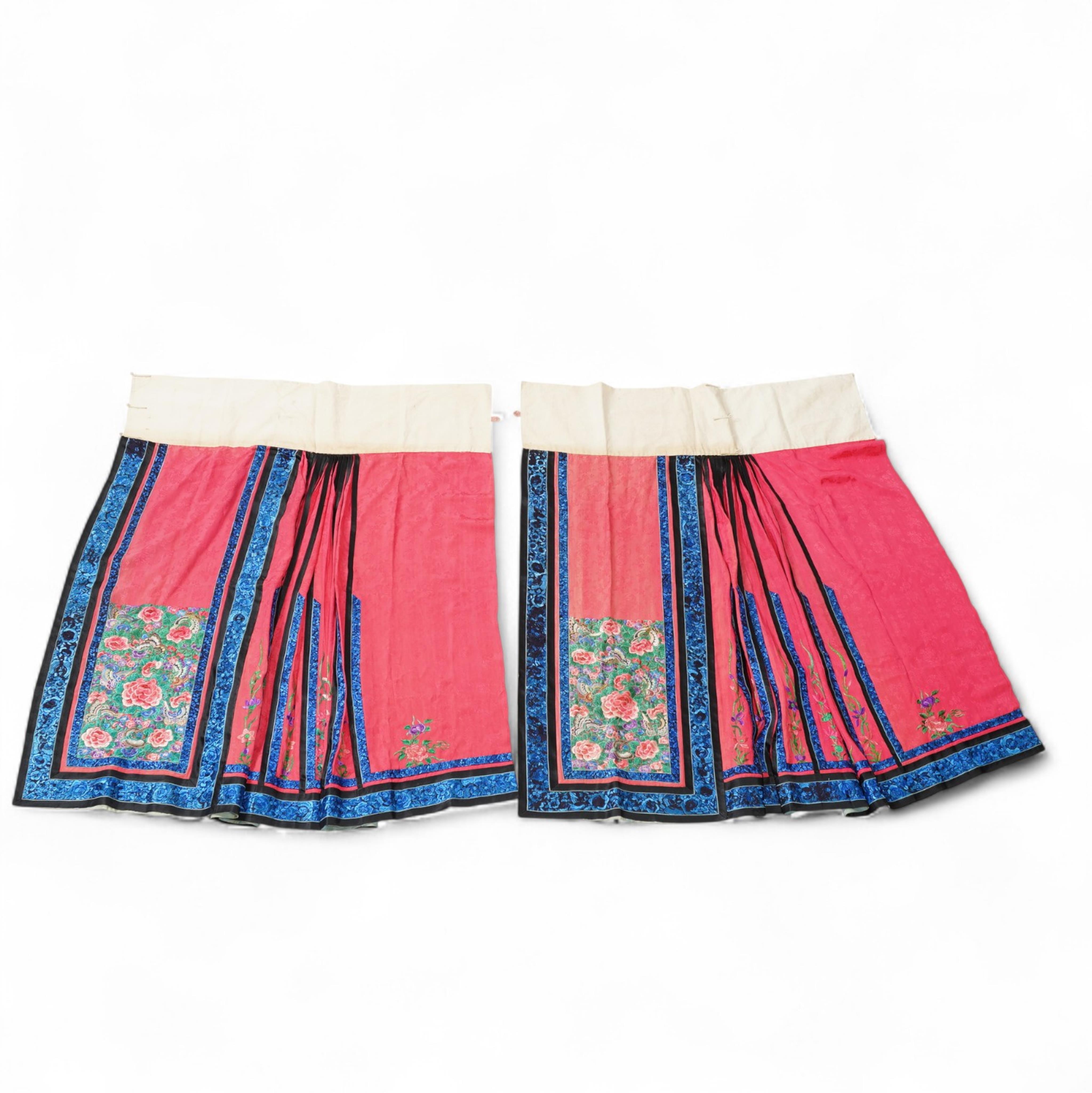 Two late 19th early 20th century Chinese wedding skirts. Made with pink silk damask, embroidered with large decorative silk floral and butterfly front panels bordered by blue embroidered black silk borders between pleats